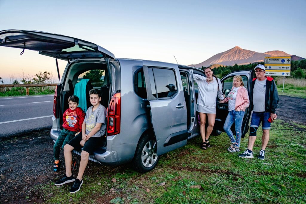 A family enjoys a scenic road trip by Mount Teide, Spain, with a van parked by the roadside.