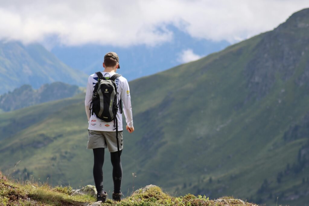 A lone hiker with a backpack stands on a mountain, enjoying the panoramic view under a cloudy sky.